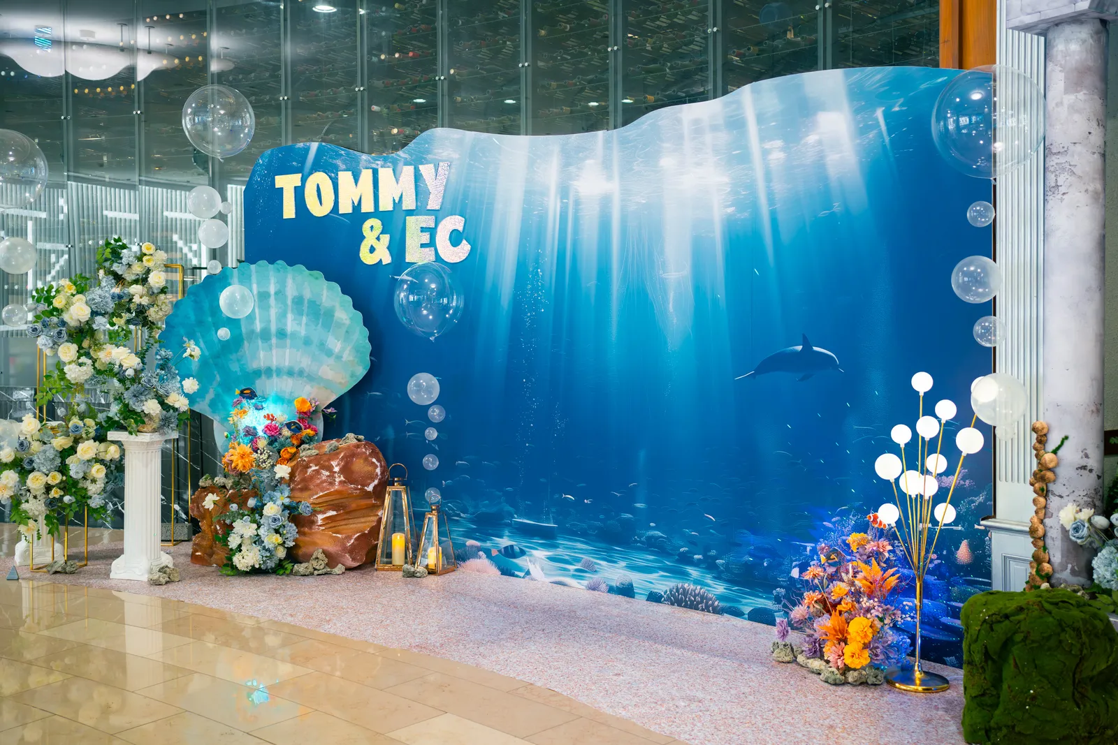 客製海洋主題震撼背板，海豚悠游於透光海水間，搭配巨型貝殼與珊瑚石花藝